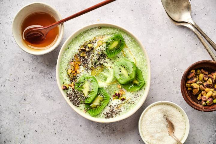 Green smoothie bowl made with banana, mango, pineapple, and yogurt in a bowl with kiwi, chia seeds, and pistachios.