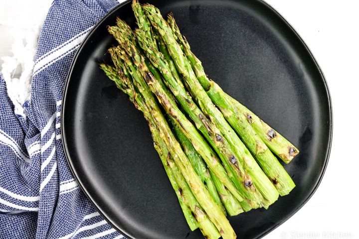 Grilled asparagus with olive oil, salt, and pepper on a black plate.