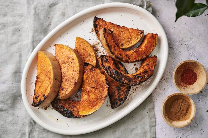 Grilled butternut squash slices on a white platter, garnished with spices, alongside two small bowls of paprika and cinnamon.