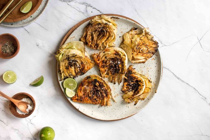 Grilled cabbage slices on a plate with grill marks with limes, salt, and grill seasoning. 