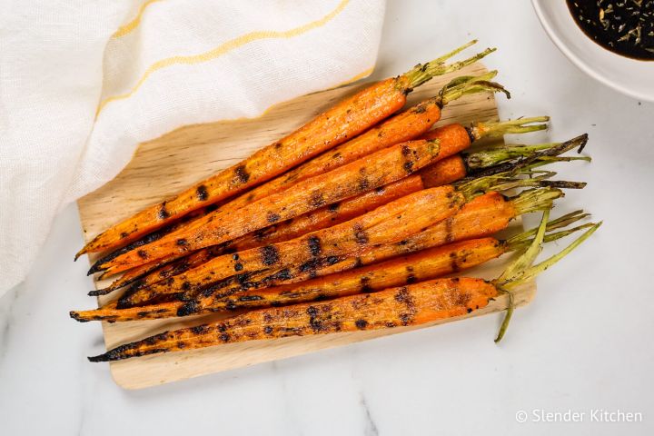 Grilled carrots with charred grill marks on a cutting board with sauce on the side.