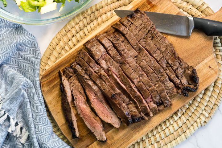 Grilled flank steak on a cutting board with a knife.