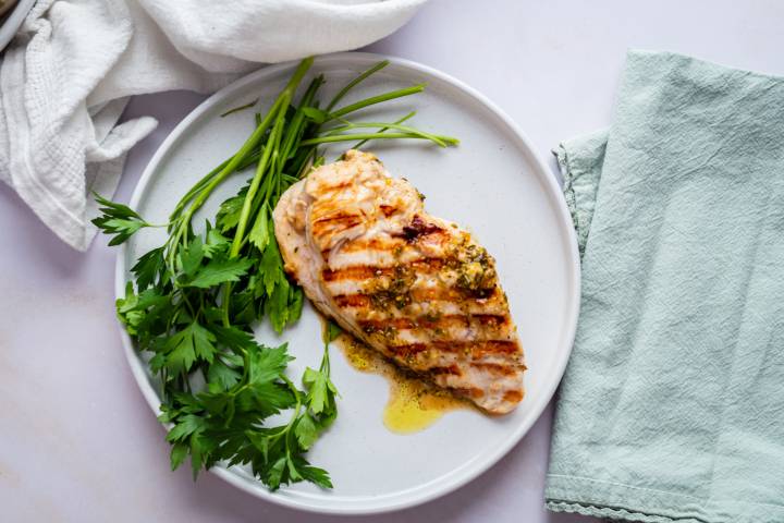 Grilled lemon pepper chicken breast on a plate with a drizzle of lemon pepper marinade and fresh parsley.