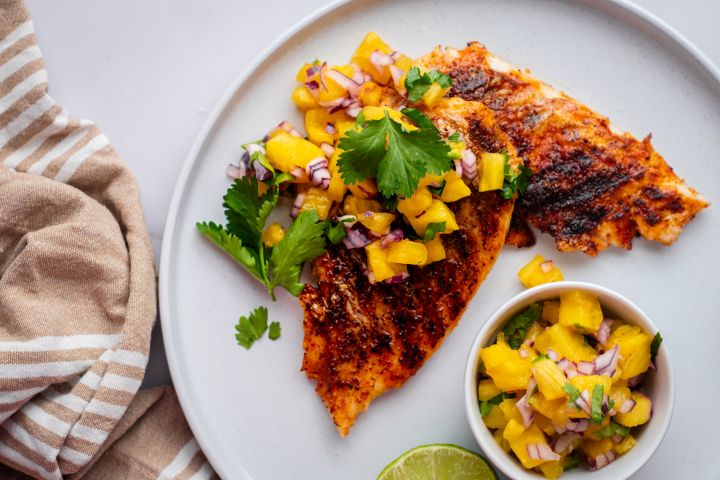 Grilled mahi mahi with paprika spice rub and pineapple salsa served on a white plate.