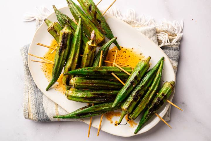 Grilled okra skewers arranged on a serving platter with smoky char marks and a sprinkle of Cajun seasoning.