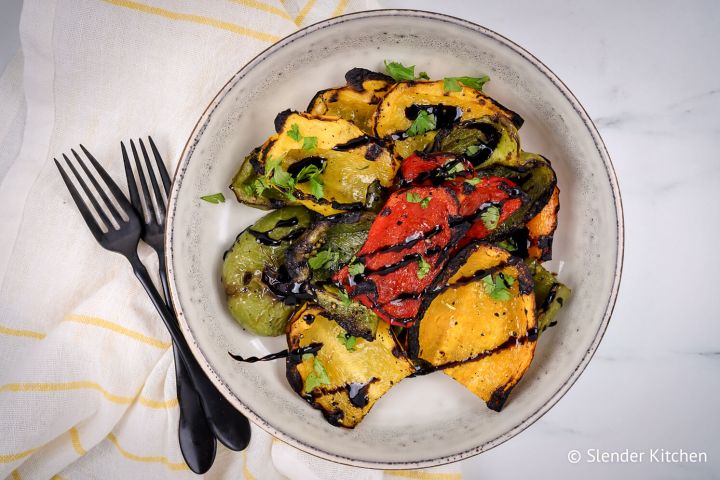 Grilled peppers with red, green, and yellow peppers with balsamic glaze on a plate.
