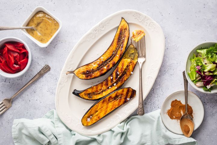 Grilled plantains with dark brown grill marks on a plate with cinnamon on the side.