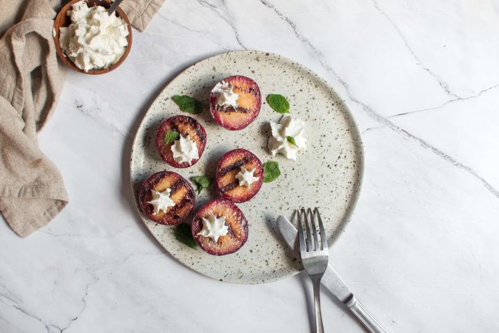 Grilled plums on a plate with honey, butter, cinnamon, and a dollop of whipped cream.