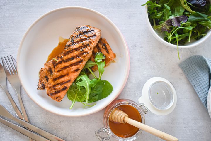 Grilled honey and lime salmon on a plate with sauce and a salad on the side.