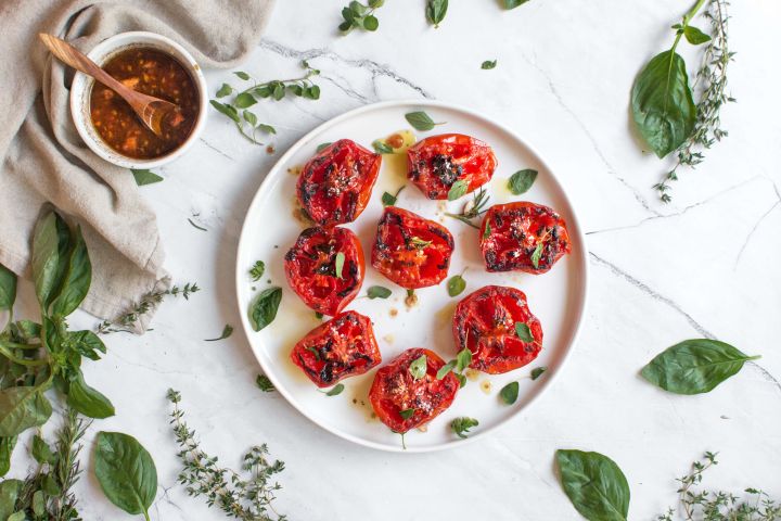 Grilled tomatoes with basil, balsamic vinegar, and garlic on a plate with fresh herbs.