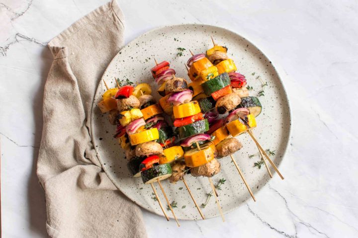 Grilled vegetable skewers with red onion, bell pepper, zucchini, summer squash, and mushrooms on wooden skewers.