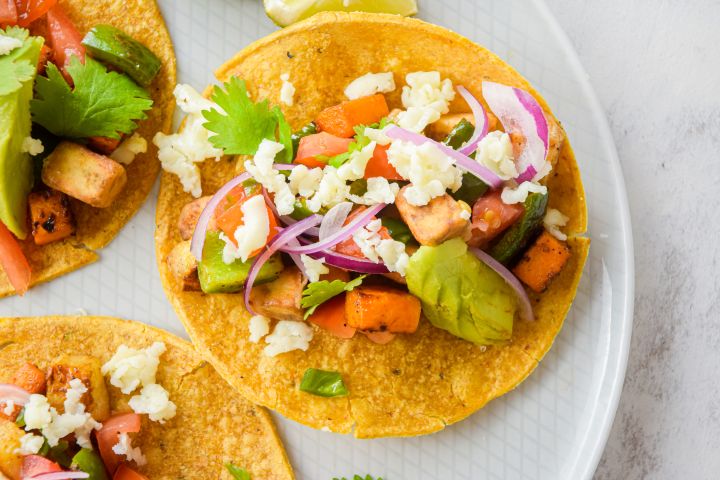 Vegetable tostadas on a plate with zucchini, eggplant, peppers, cheese, and avocado.