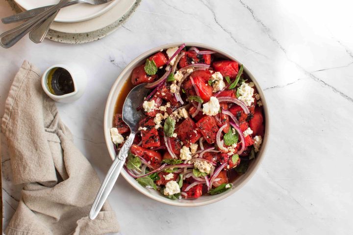 Grilled watermelon salad with feta cheese, fresh mint, basil, red onion, and balsamic vinegar in a bowl. 