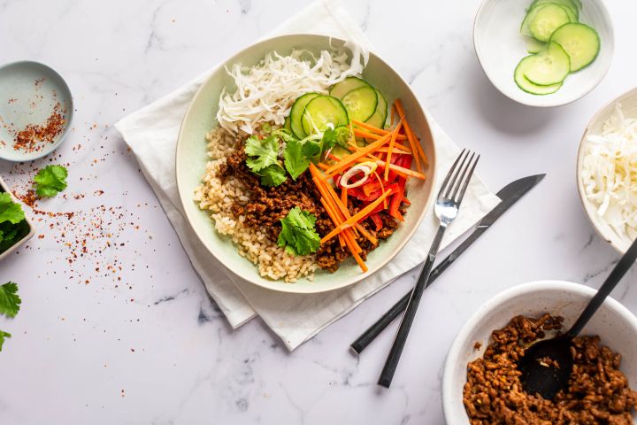 Ground beef bulgogi bowls with Korean flavored beef, cucumbers, carrots, red peppers, cabbage, and rice in a bowl. 