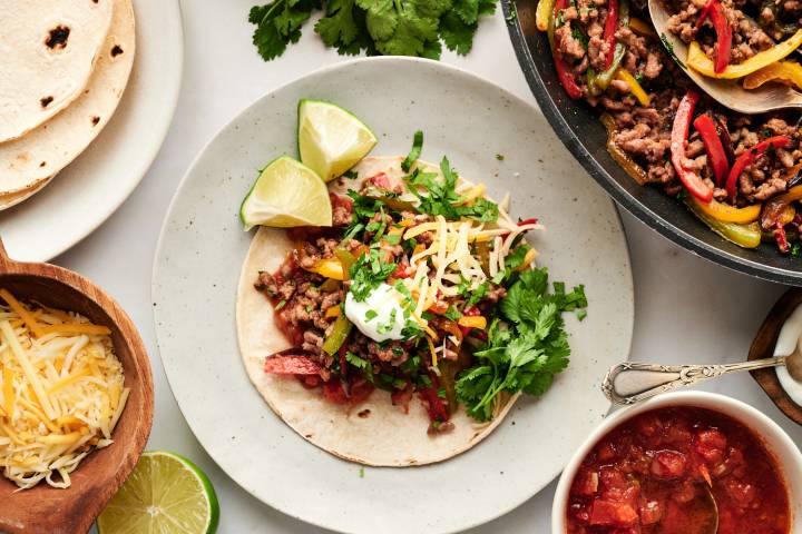 Ground beef fajitas with seasoned beef, bell peppers, onions, cilantro, cheese, and sour cream on flour tortillas.