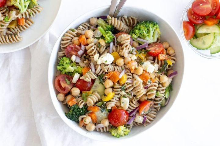 Vegetable pasta salad with cooked whole wheat pasta, chopped fresh vegetables, chickpeas, and feta cheese topped with lemon dressing.