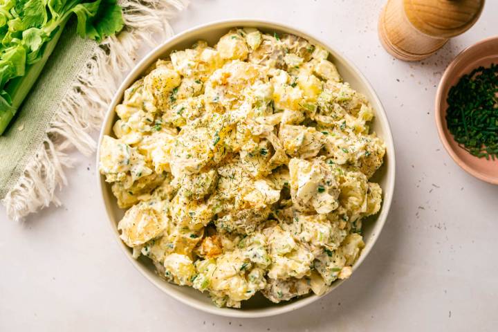 Close-up of chunky potato salad garnished with dill and chives, served in a wide bowl on a green striped napkin.