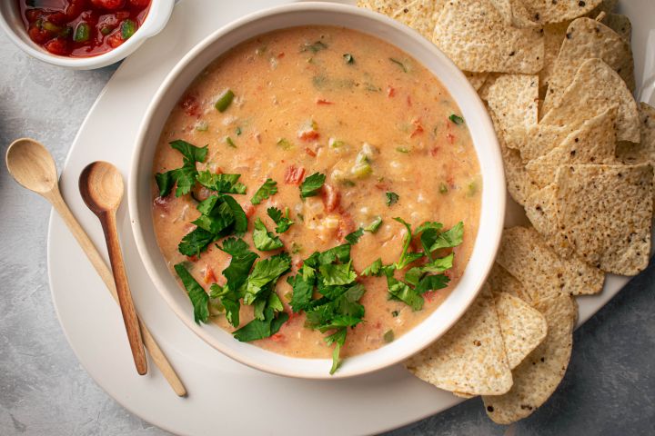 Healthy queso dip with melted cheddar cheese, diced tomatoes, and jalapeños in a bowl with tortilla chips.