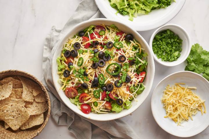 Healthy taco dip with seasoned cream cheese, refried beans, lettuce, salsa, and shredded cheese in a bowl with tortilla chips.