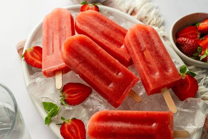 Platter of healthy watermelon popsicles on ice, garnished with fresh strawberries and mint for a refreshing summer dessert.