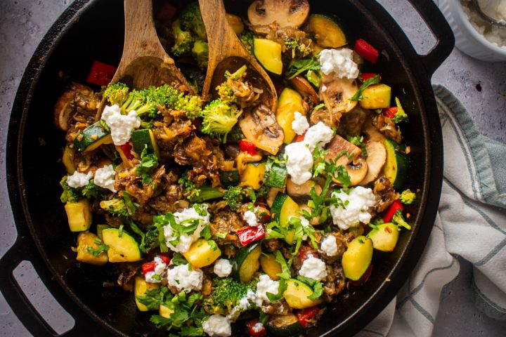 Hippie hash with hash browns, zucchini, mushrooms, broccoli, and red peppers in a skillet.