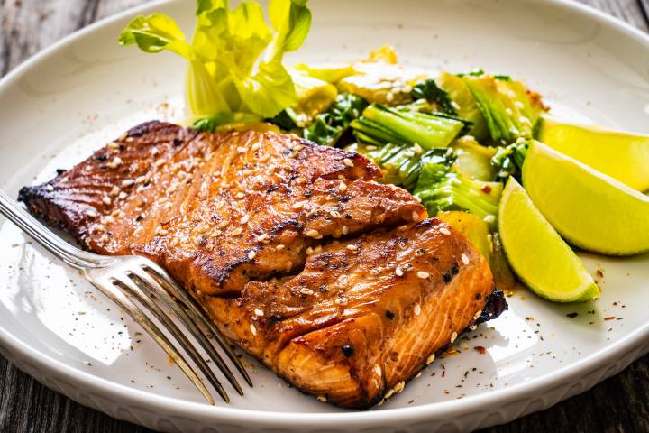 Hoisin salmon with caramelized edges on a plate with bok choy and limes.