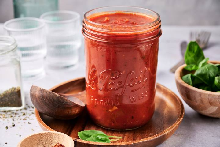 Homemade marinara sauce in a glass jar with flecks of garlic and fresh basil.