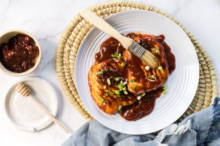 Honey chipotle grilled chicken on a plate with sliced green onions and honey chiptole sauce.