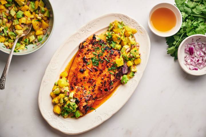 Honey chipotle salmon with mango, cucumber, and red onion salsa served on a plate with cilantro on the side.