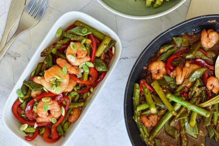 Honey garlic shrimp stir fry on a plate with asparagus, snap peas, red peppers, and stir fry sauce.