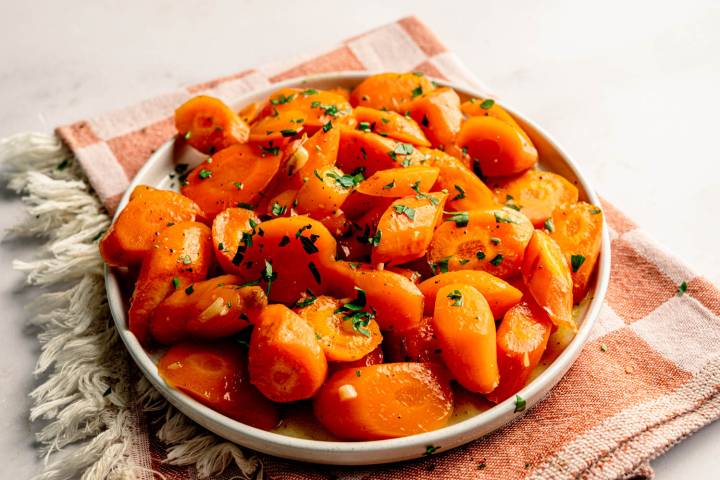 Close-up of roasted honey glazed carrots in a serving bowl with fresh parsley on a checkered kitchen towel.