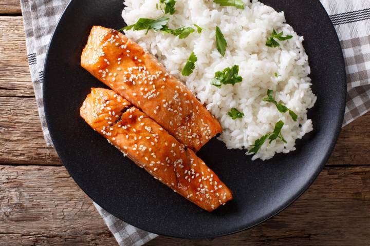 Honey soy salmon with glaze served on a bed of white rice with green onions and sesame seeds.