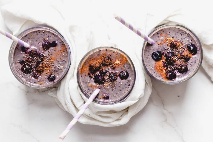 Blueberry banana smoothie served in three glasses with fresh blueberries and cinnamon on top.