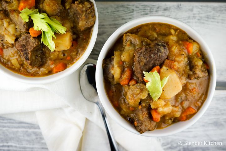 Instant pot beef stew with tender beef, carrots, and potatoes in two bowls with fresh herbs.