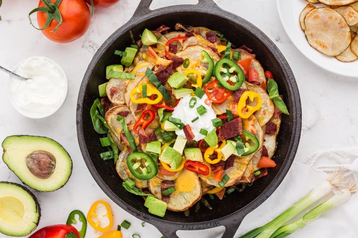 Irish Nachos with crispy baked potato chips, bacon, cheese, avocado, peppers, and sliced green onions in a cast iron skillet.
