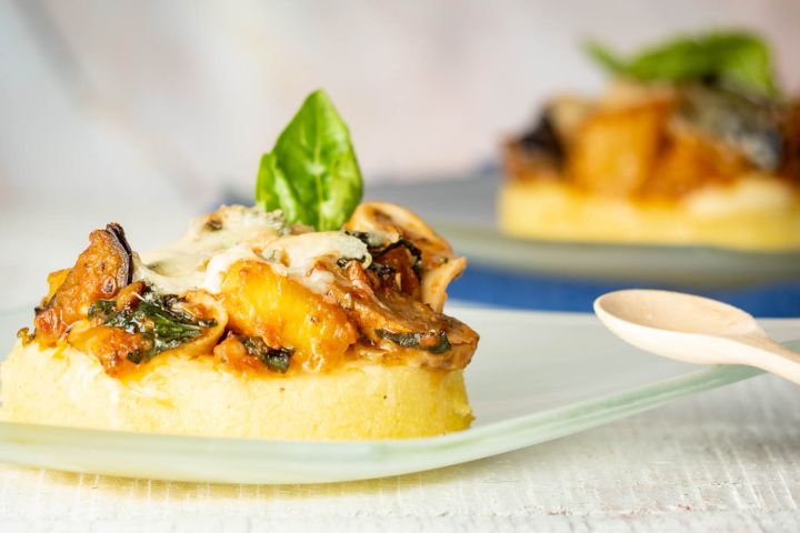 Baked polenta with tomato sauce, vegetables, and cheese with fresh basil.