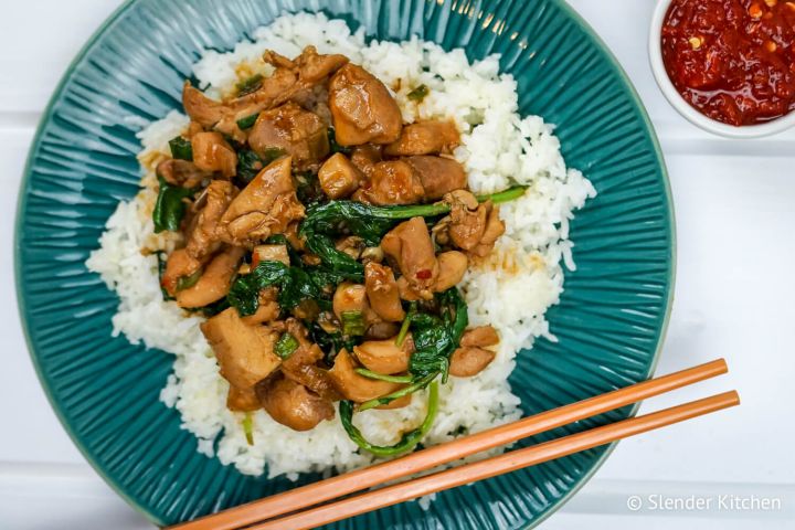 Korean chicken with spinach, rice, and hot sauce on a plate with chopsticks.