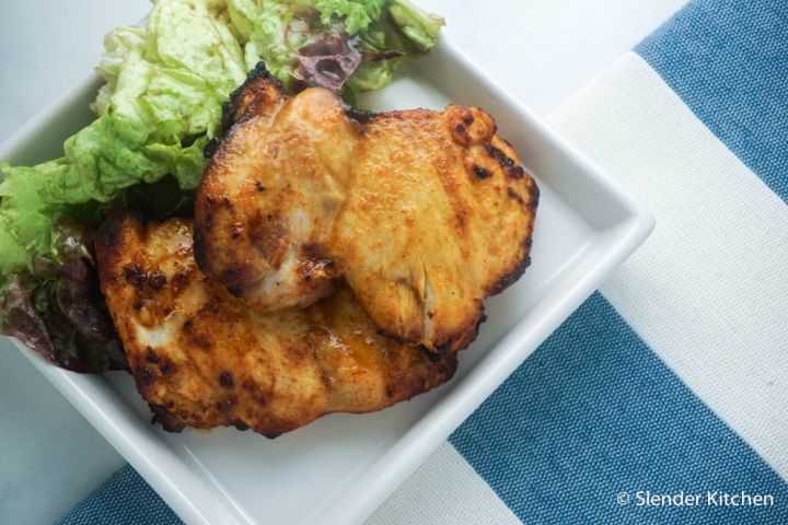 Lemon paprika chicken thighs on a plate with greens.