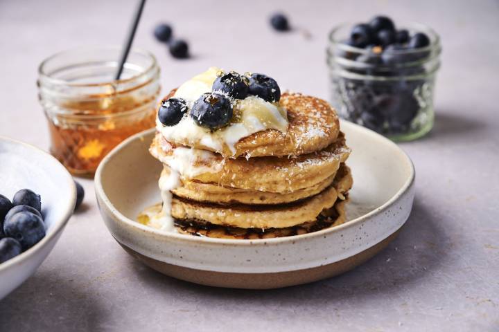 Low carb almond flour pancakes on a plate with blueberries, yogurt, and maple syrup.