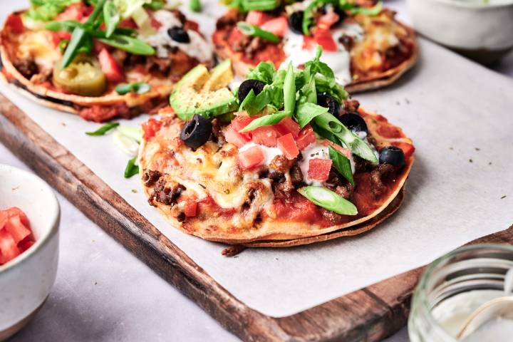 Mexicna pizzas with ground beef, refried beans, crispy corn tortillas, and melted cheese topped with lettuce, tomatoes, jalapenos, and sour cream.