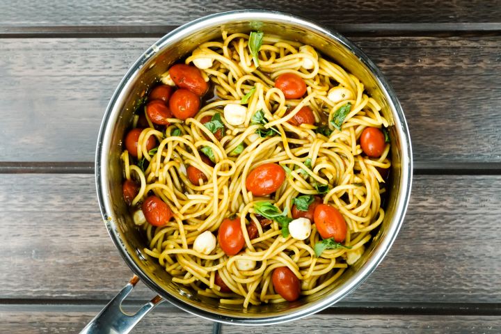 Caprese pasta in a pot with cherry tomatoes, mozzarella cheese, and basil.