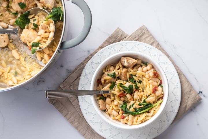 Orzo pasta with chicken breast, spinach, tomatoes, and white beans served in a bowl with Parmesan cheese.