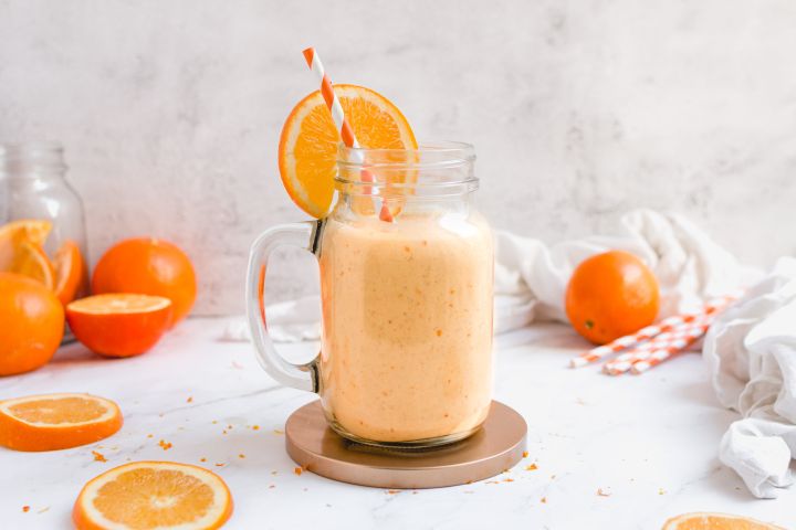 Orange creamsicle smoothie made with bananas and oranges in a glass with an orange striped straw.