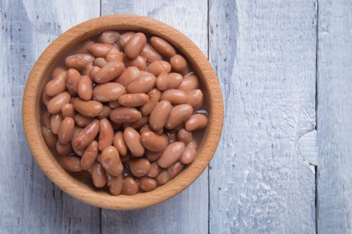 Oven baked pinto beans in a bowl on a white wooden board.