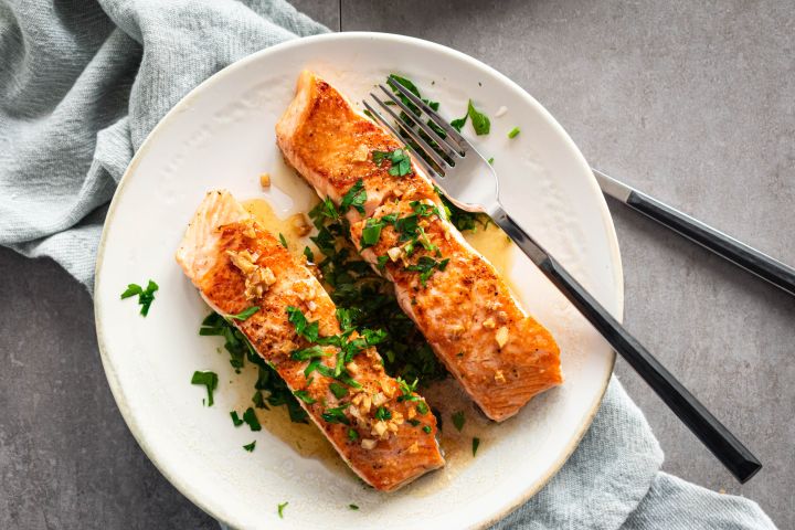 Pan seared salmon with garlic, lemon, and butter served on a plate with a lettuce and tomato salad.