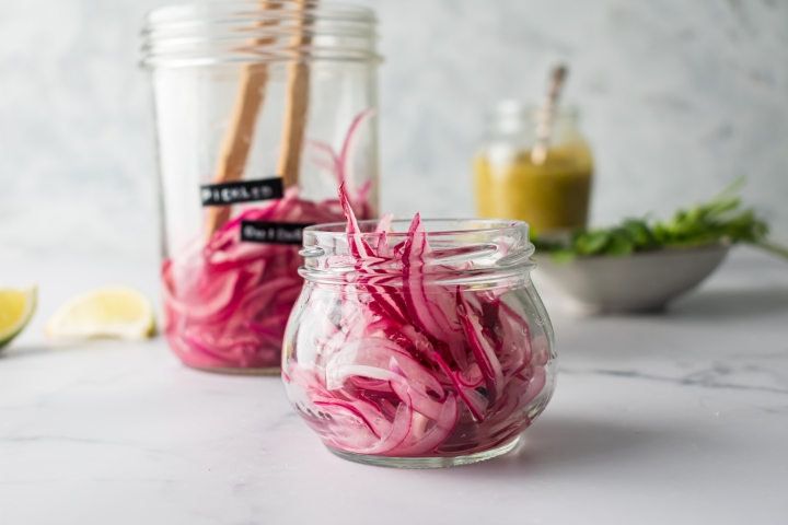 Pickled red onions in a glass jar with lime juice, vinegar, and peppercorns. 