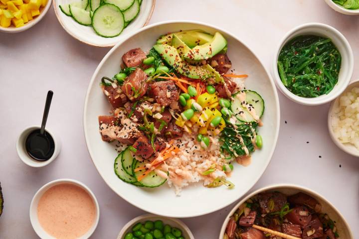 Poke bowls with ahi tuna poke, rice, seaweed salad, avocado, spicy mayo, cucumbers, carrots, and sesame seeds.