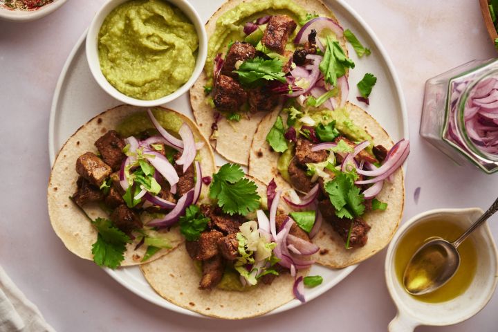 Pork tacos with crispy pork, red onions, cilantro, and avocado on a plate.