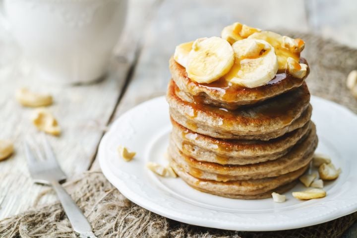 Banana oatmeal pancakes served in a stack with sliced bananas and maple syrup.