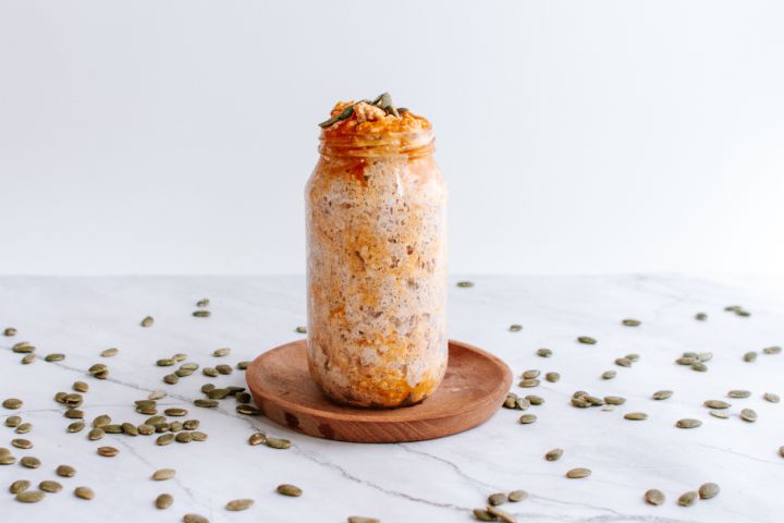 Pumpkin overnight oatmeal in a mason jar with pumpkin seeds, pumpkin puree, and cinnamon.